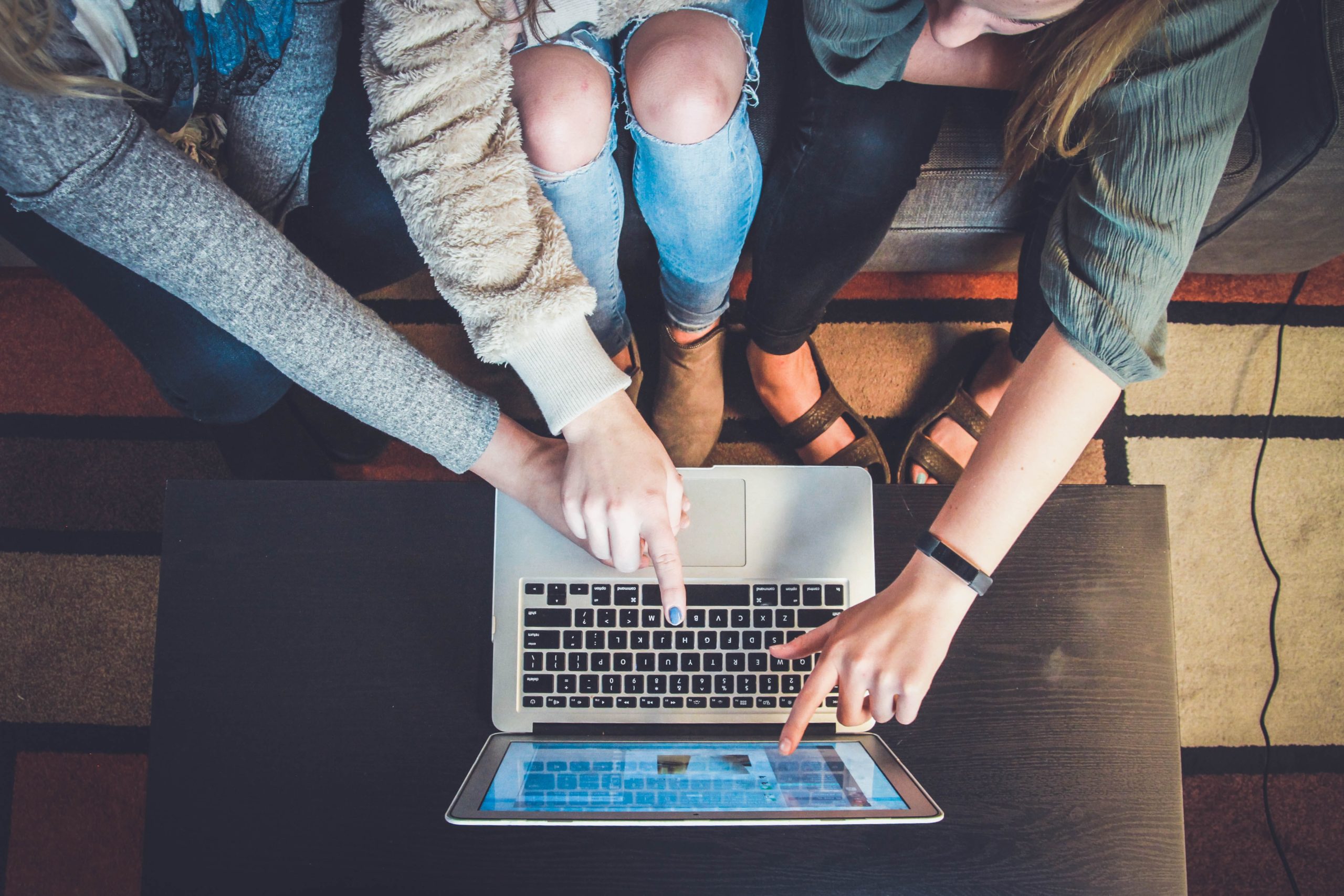 Several hands point at the screen of a laptop. 